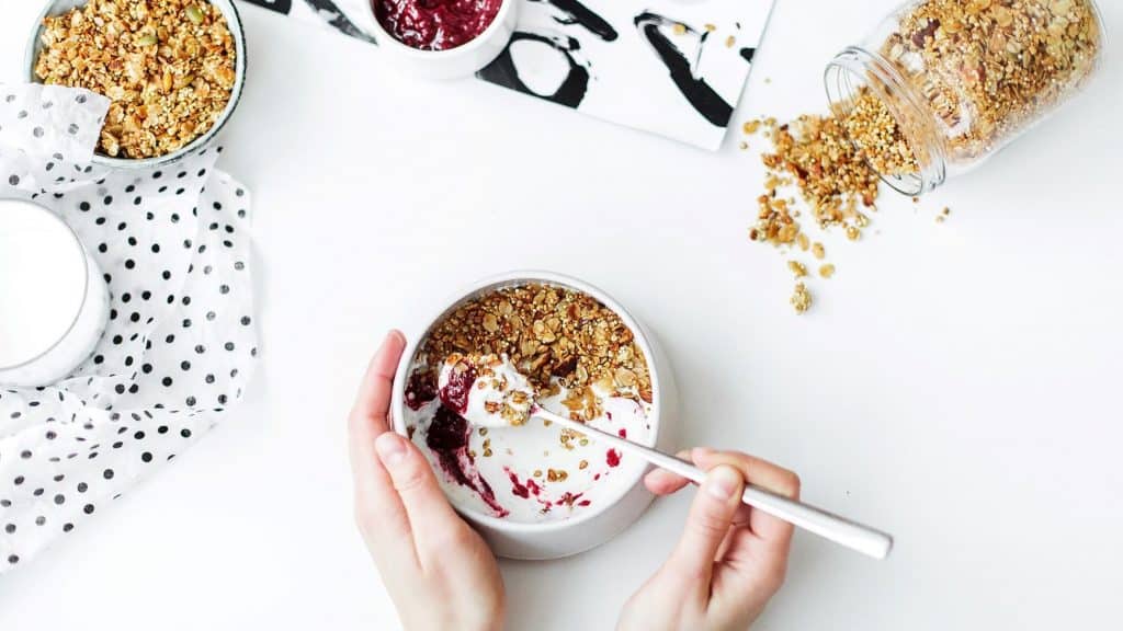 hand mixing granola into a bowl of yogurt and strawberries