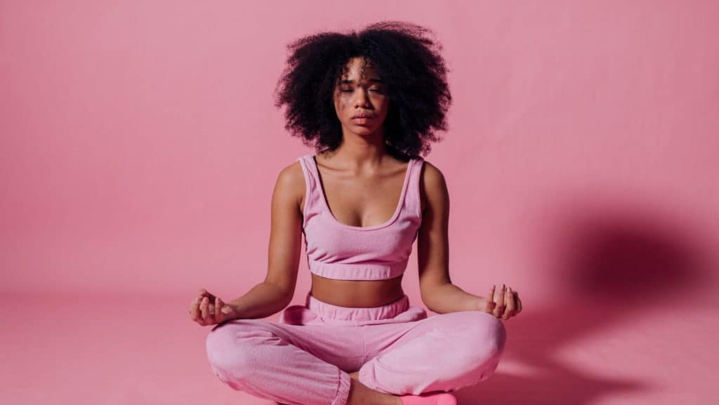 woman meditating in front of a pink background