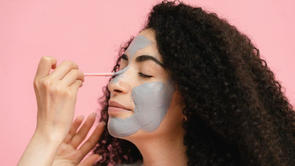 woman applying face mask with pink background