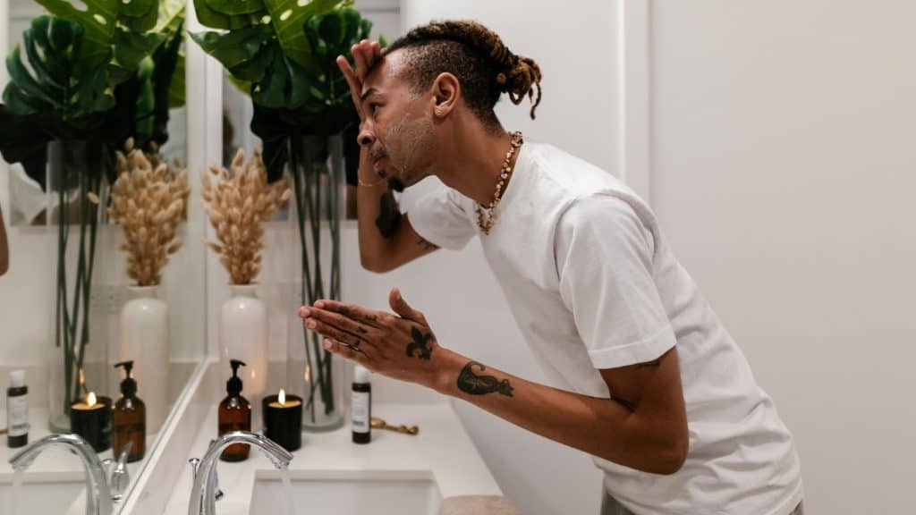 Black man using skin care products in a mirror